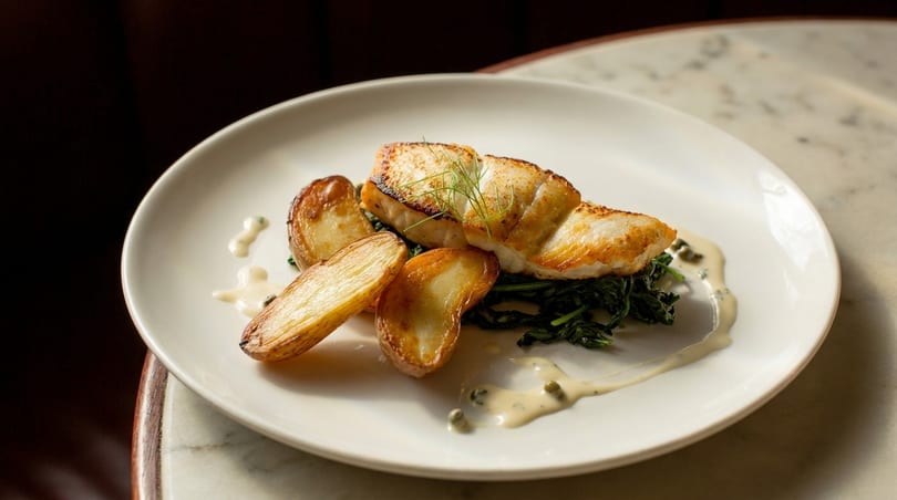 Pan-seared fish with roasted potatoes, spinach, and a creamy sauce on a white plate.