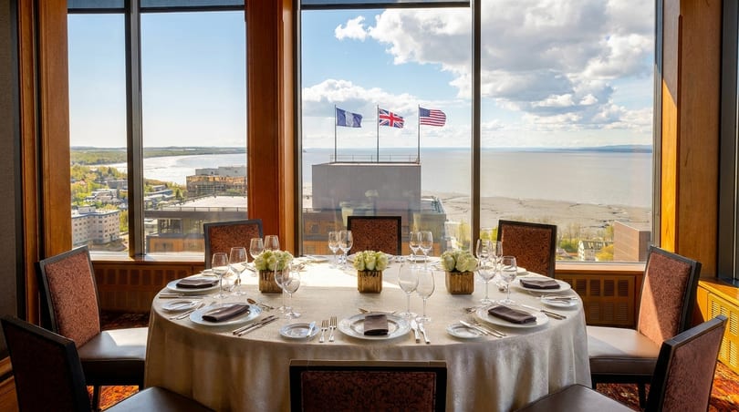 A formal dining table set for eight with a panoramic view of a city and bay.
