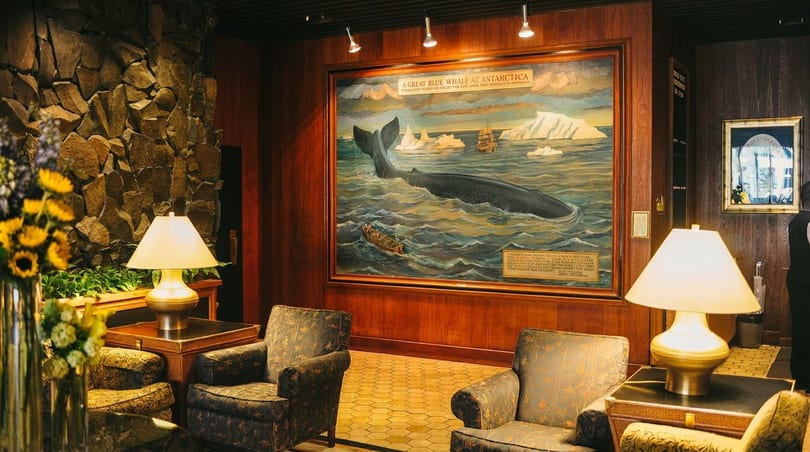 Lobby with a large whale painting, two armchairs, lamps, and a stone wall.