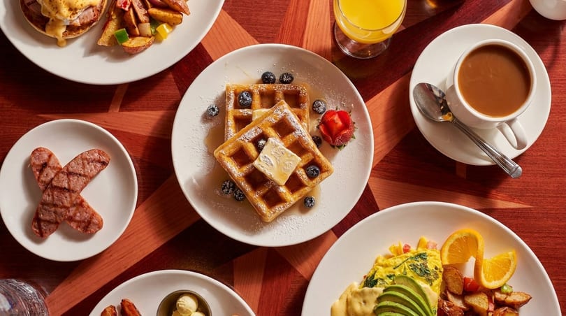 Overhead view of a breakfast spread with waffles, eggs benedict, sausage, coffee, and orange juice.
